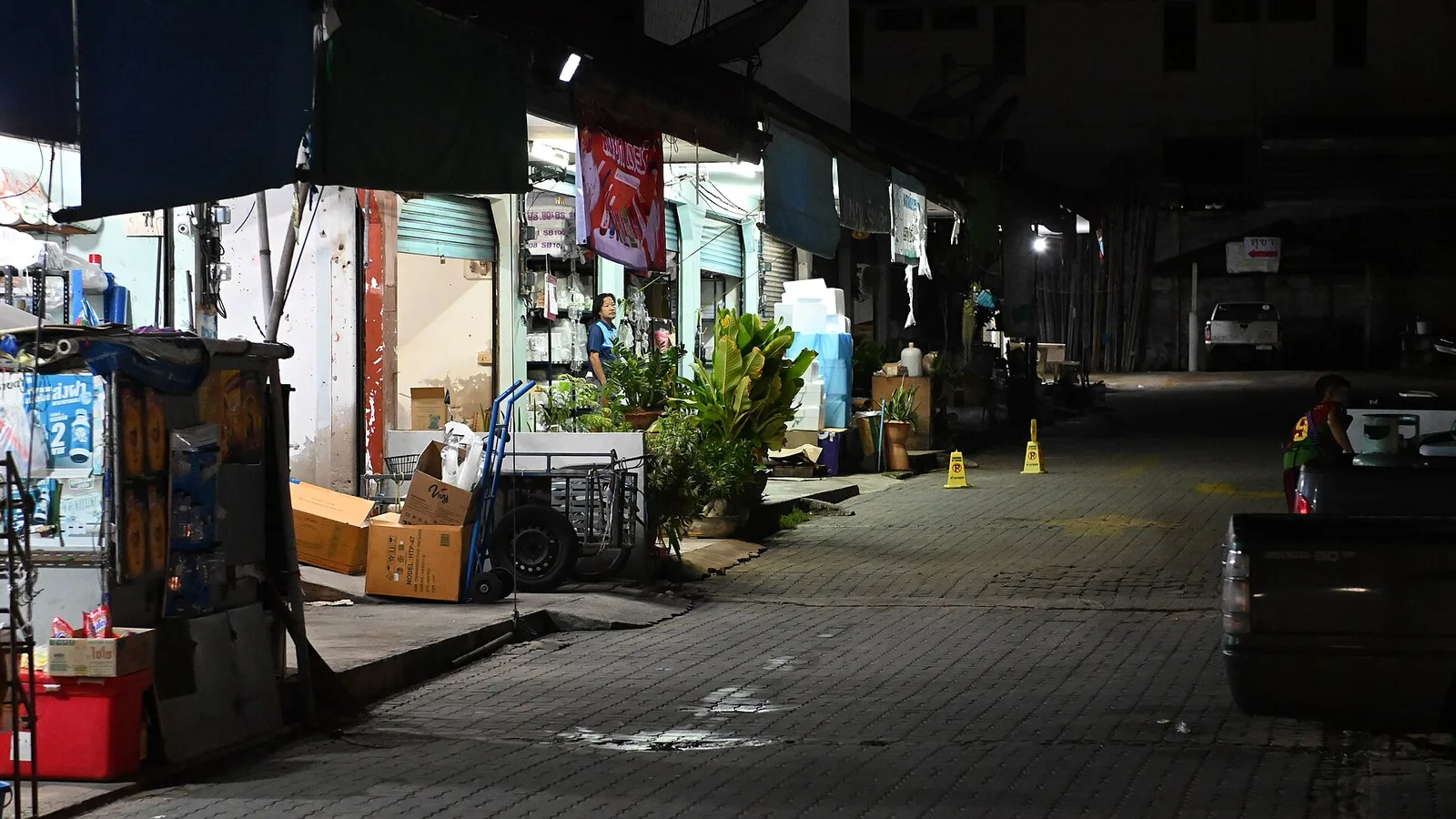 DFC 1772 Dimly lit row of closed storefronts and market stalls along a quiet empty street at night