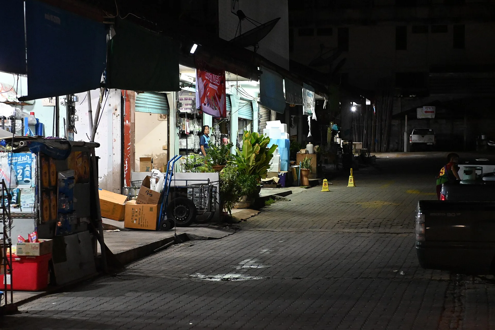 DFC 1772 Dimly lit row of closed storefronts and market stalls along a quiet empty street at night